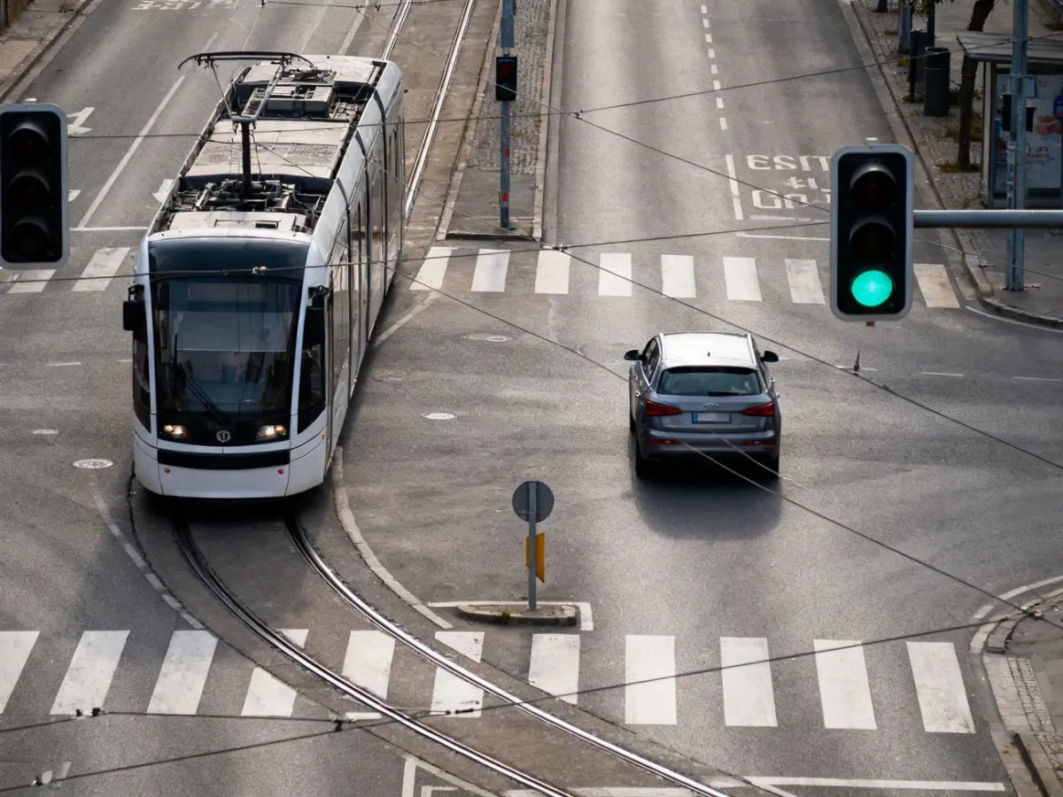 Tram skręcający na skrzyżowaniu z sygnalizacją, podczas gdy samochód jedzie prosto